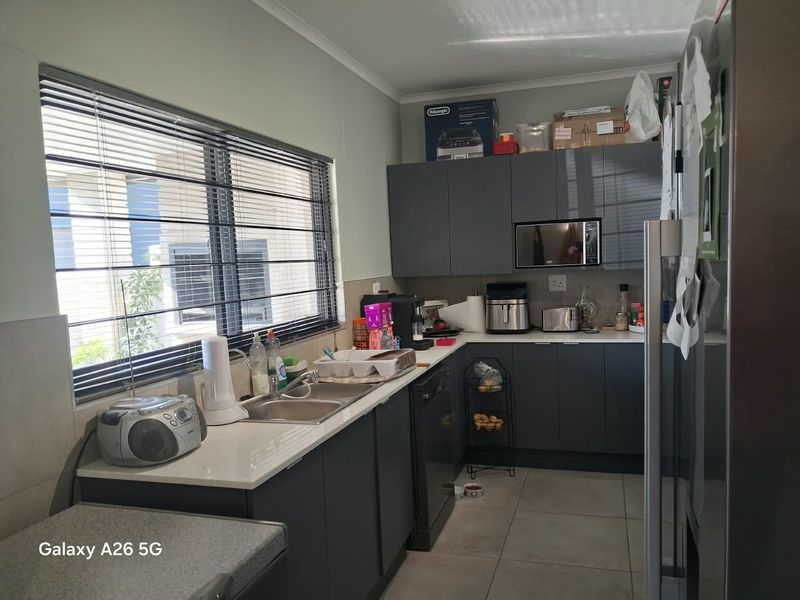 A functional kitchen featuring modern dark grey cabinetry, stone countertops, a double basin sink, and tiled flooring with ample natural light.