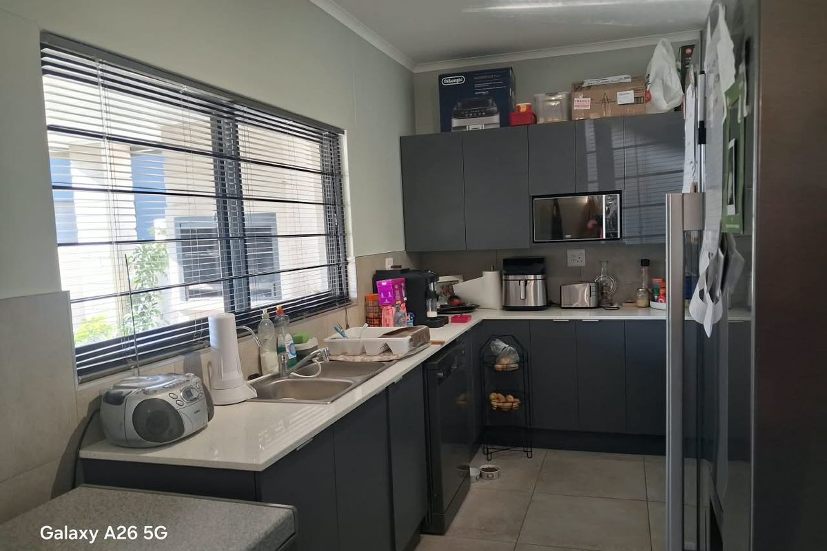A functional kitchen featuring modern dark grey cabinetry, stone countertops, a double basin sink, and tiled flooring with ample natural light.