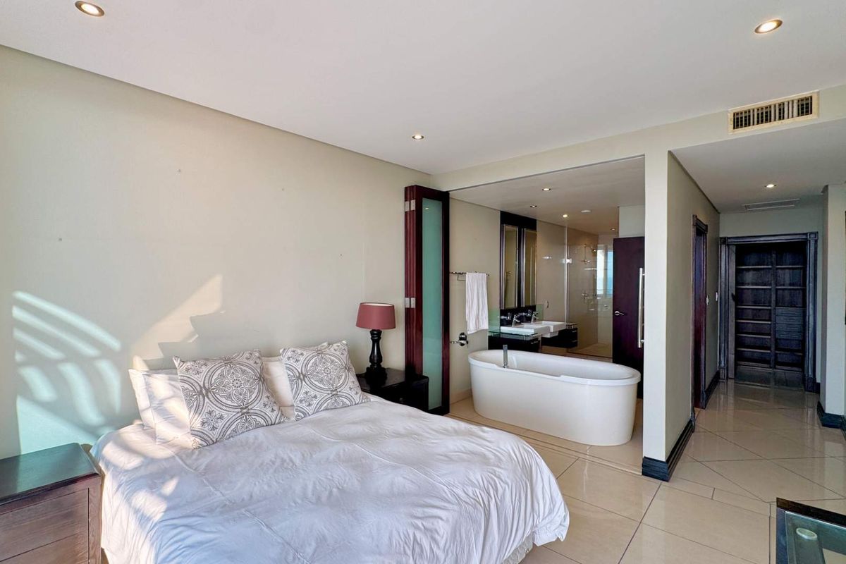 Spacious bedroom featuring an open-plan en-suite bathroom with a modern freestanding bathtub, tiled flooring, and recessed lighting.