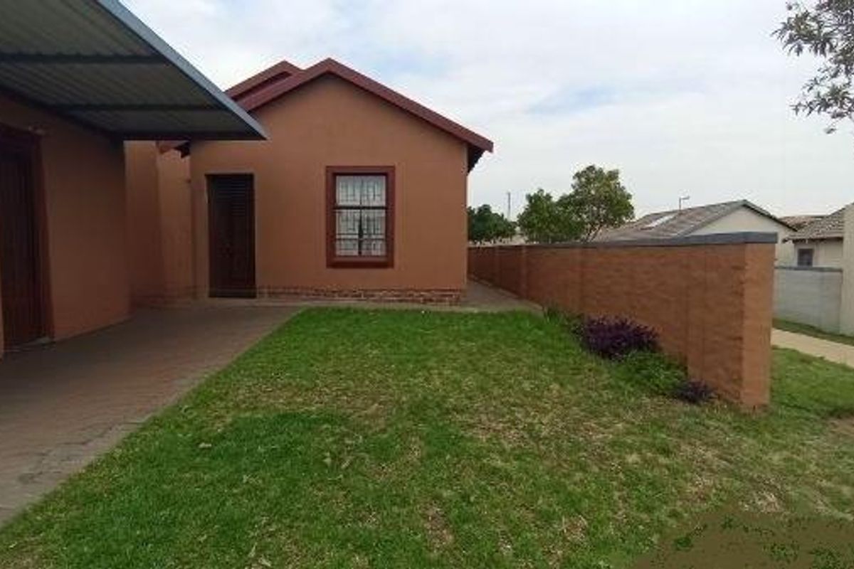 A view of the exterior rear of the house, featuring a paved patio area, a small lawn, and a perimeter boundary wall.
