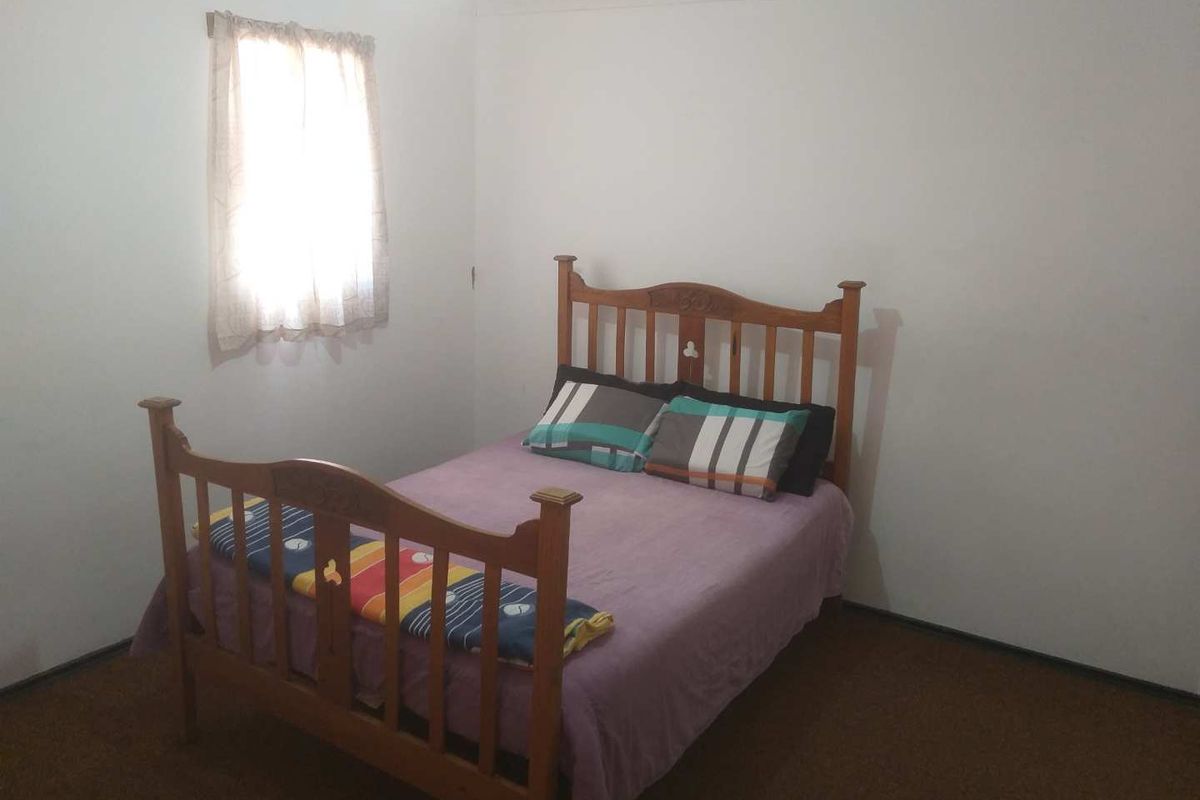 A simple bedroom featuring carpet flooring and a single window, providing a functional space for rest.
