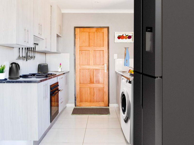A functional kitchen featuring light-toned cabinetry, tiled flooring, and a built-in oven, with direct access to an exterior timber door.
