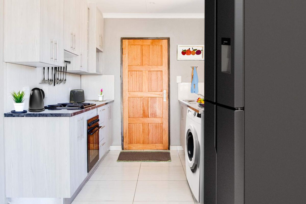 A functional kitchen featuring light-toned cabinetry, tiled flooring, and a built-in oven, with direct access to an exterior timber door.