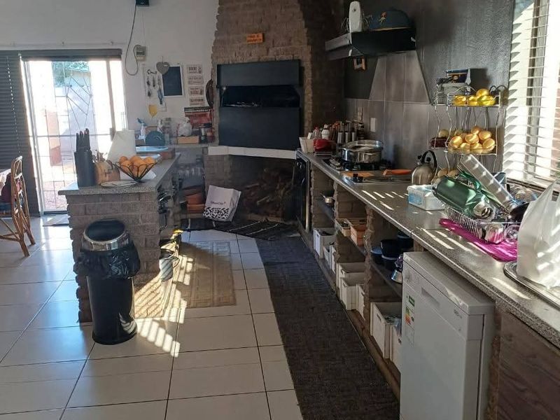Kitchen featuring a prominent built-in brick fireplace, tiled flooring, and functional cabinetry with an integrated extractor fan and access to an outdoor area.