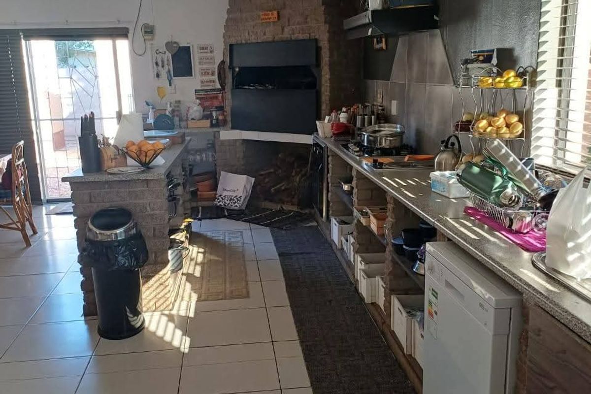Kitchen featuring a prominent built-in brick fireplace, tiled flooring, and functional cabinetry with an integrated extractor fan and access to an outdoor area.