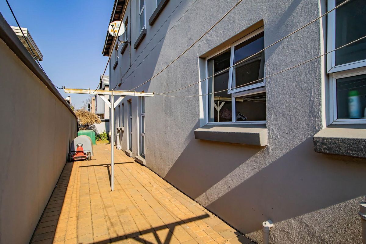 A side exterior view of the property featuring a paved walkway, boundary wall, and fixed washing line infrastructure.