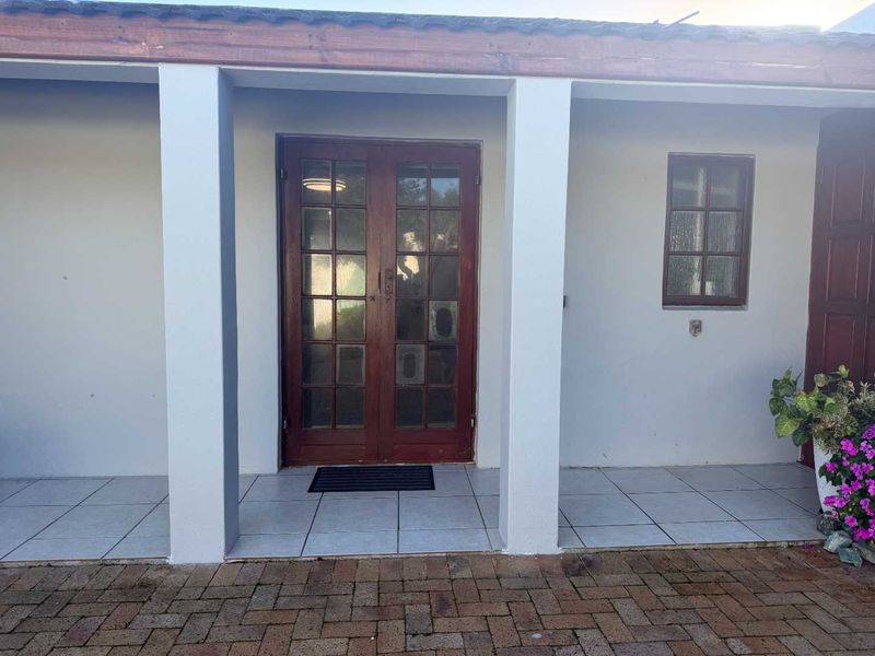 A covered patio area featuring tiled flooring, concrete support pillars, and wooden french doors leading into the apartment.