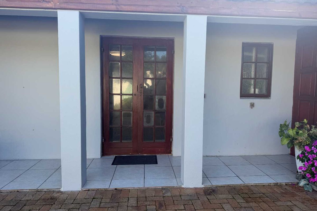 A covered patio area featuring tiled flooring, concrete support pillars, and wooden french doors leading into the apartment.