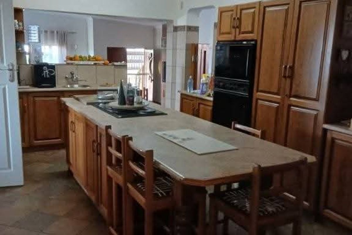 Spacious kitchen featuring extensive wooden cabinetry, a large central island with integrated hob, and durable tiled flooring.