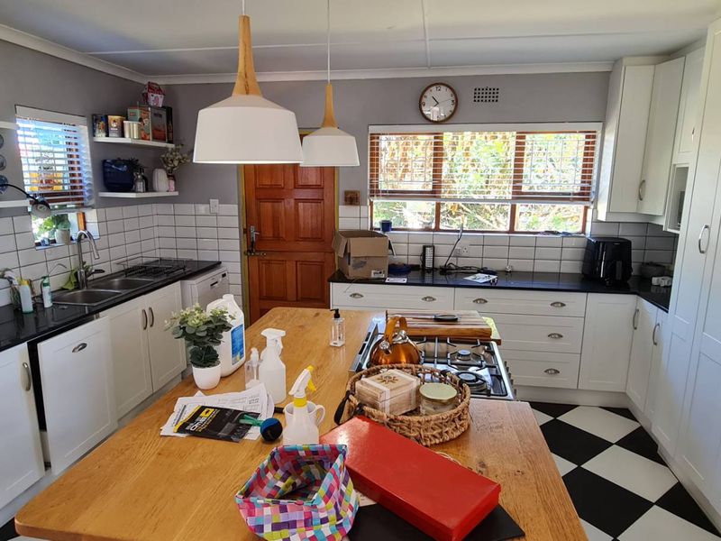A well-appointed kitchen featuring white shaker cabinetry, black granite countertops, subway tile backsplash, a central timber island, and classic checkerboard flooring.