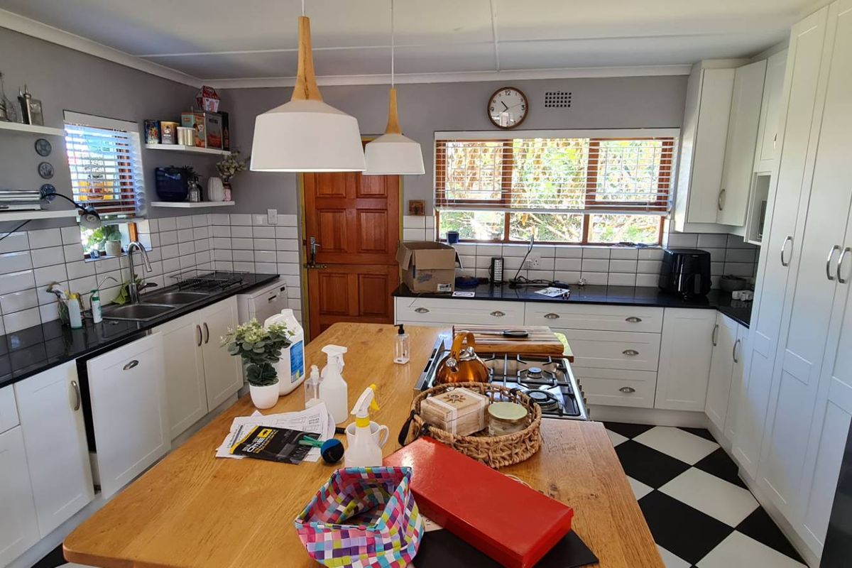A well-appointed kitchen featuring white shaker cabinetry, black granite countertops, subway tile backsplash, a central timber island, and classic checkerboard flooring.
