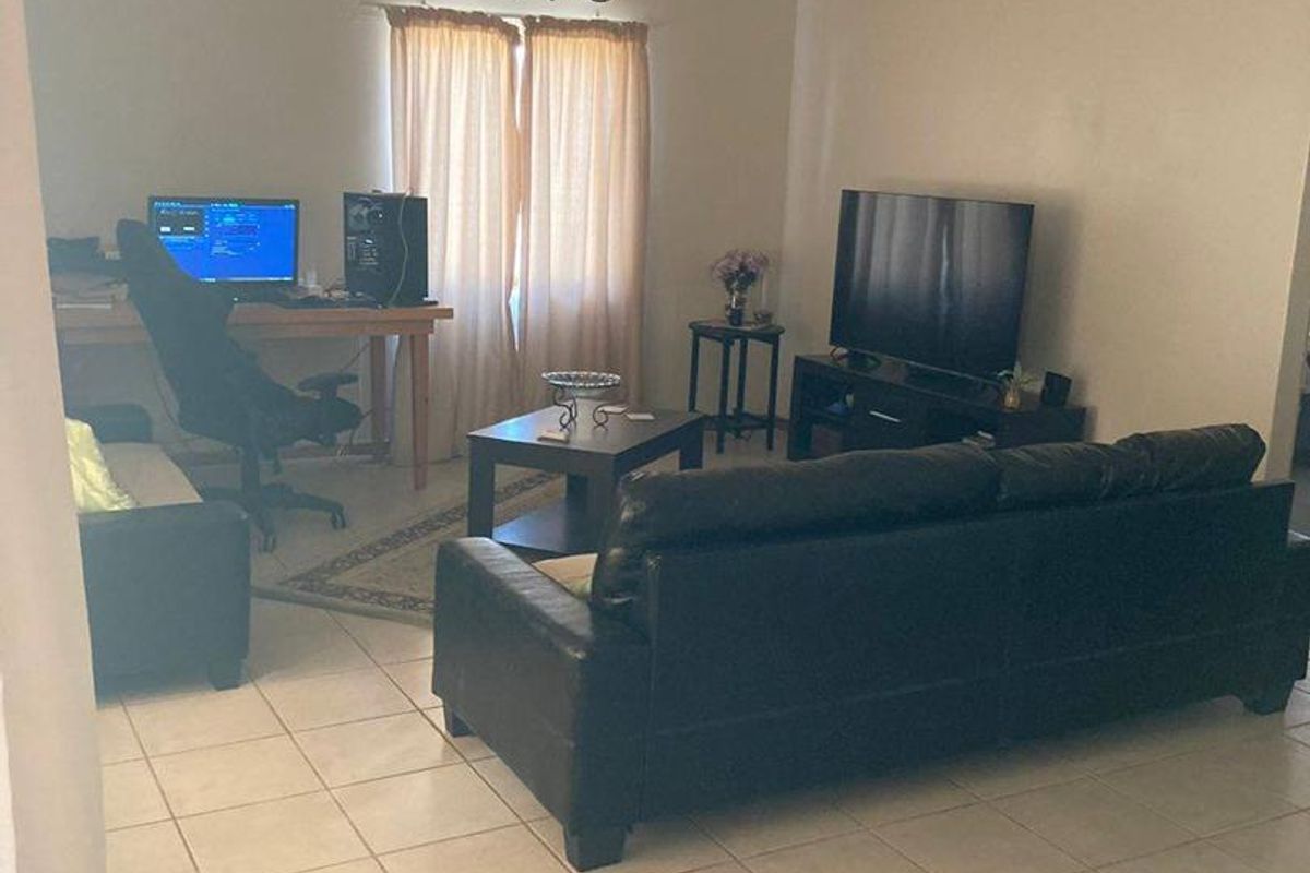 A functional living room featuring tiled flooring, a ceiling-mounted light fixture, and a wall-mounted air conditioning unit.