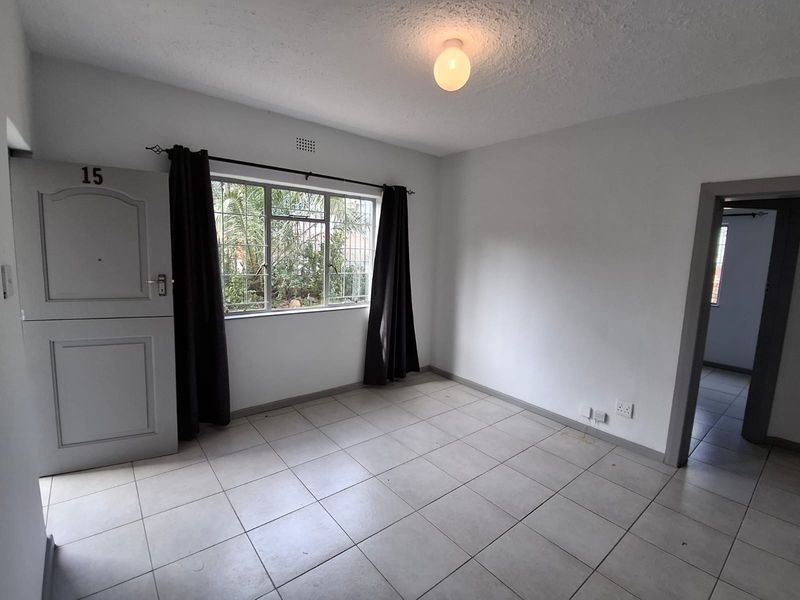 An empty living room featuring tiled flooring, a security gate, and window security bars, offering a blank canvas for personalization.