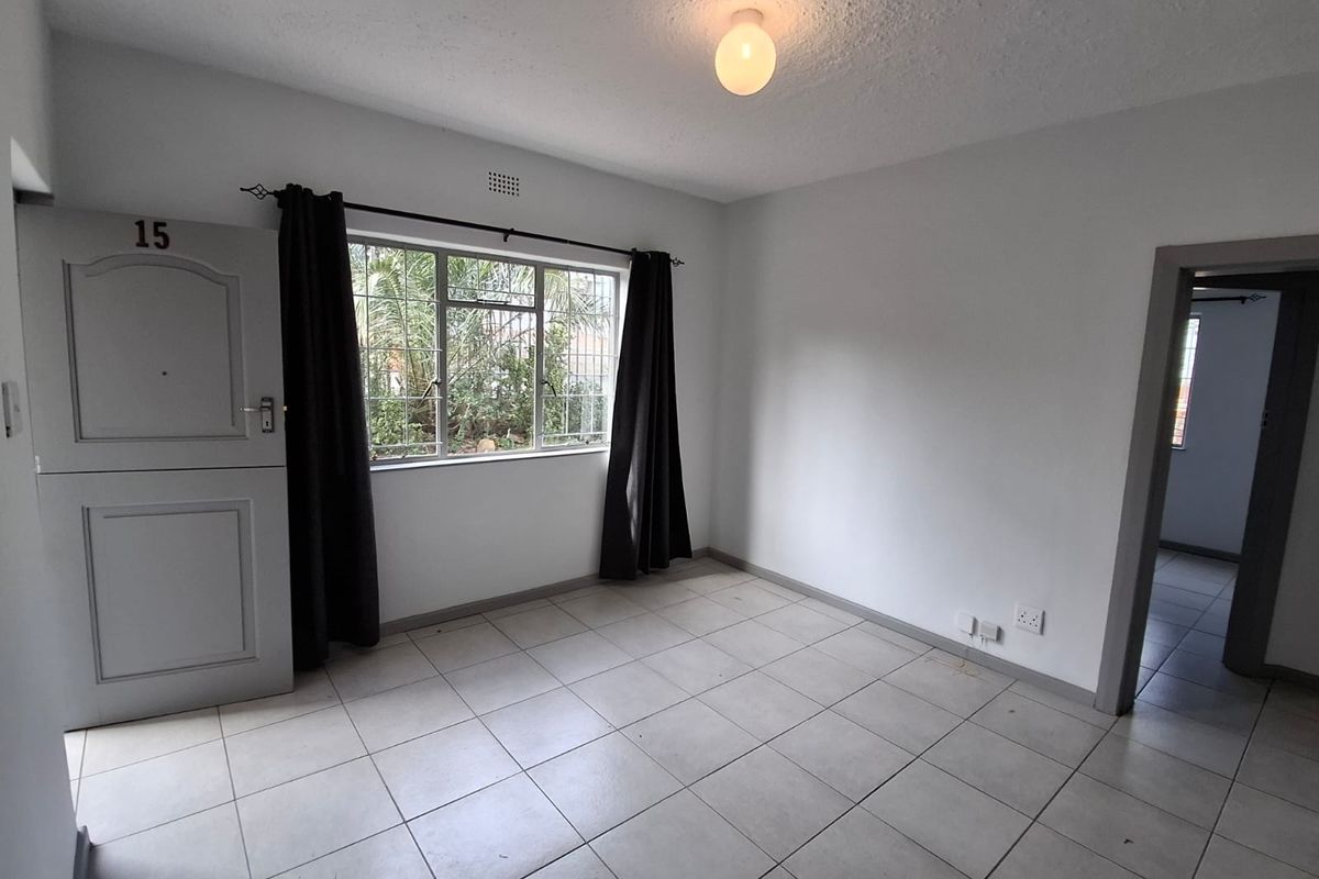An empty living room featuring tiled flooring, a security gate, and window security bars, offering a blank canvas for personalization.