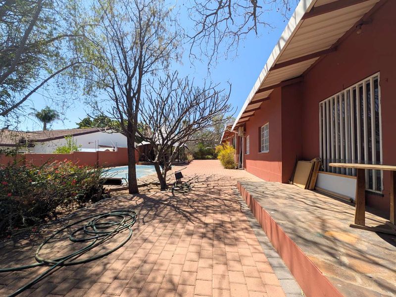 Rear exterior view featuring a paved patio area, swimming pool, and boundary wall with electric fencing.