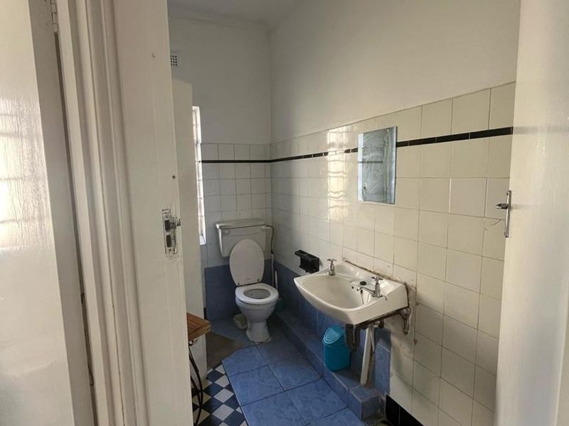 A dated bathroom featuring a wall-mounted basin, toilet, and classic checkered floor tiling, offering potential for a modern renovation.