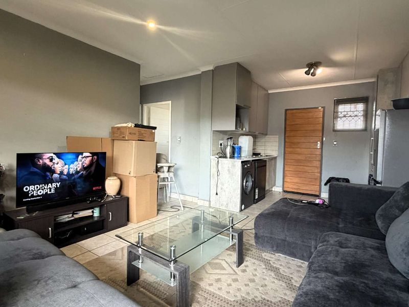 Open-plan living area featuring tiled floors, recessed lighting, and a compact kitchen space with built-in cabinetry.