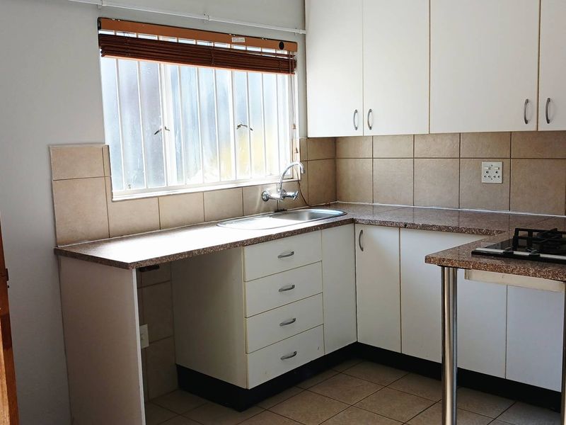 A functional kitchen featuring white cabinetry, granite-look laminate countertops, a stainless steel sink, and a built-in gas hob with tiled backsplash.