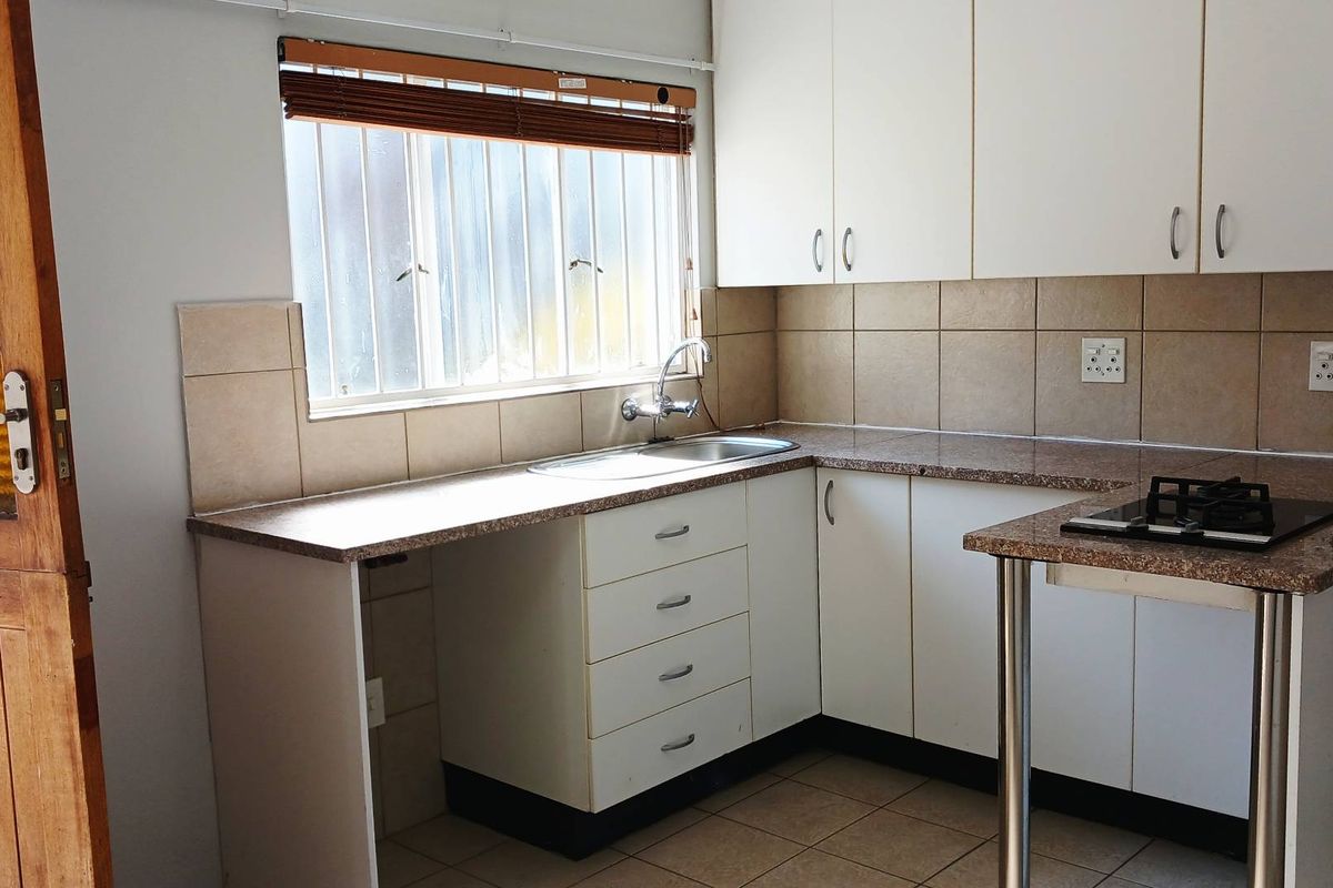 A functional kitchen featuring white cabinetry, granite-look laminate countertops, a stainless steel sink, and a built-in gas hob with tiled backsplash.