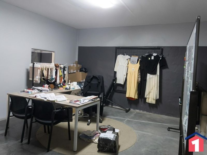 A functional industrial-style office space featuring concrete flooring, neutral wall tones, and a wall-mounted display grid for versatile use.