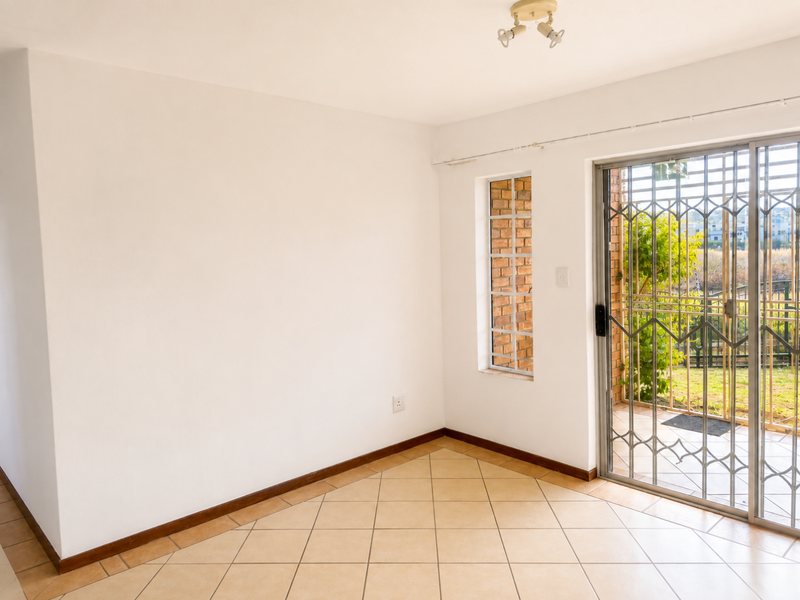 An empty living area featuring ceramic tile flooring, exposed brick detailing around the window, and a sliding glass door with a security gate.