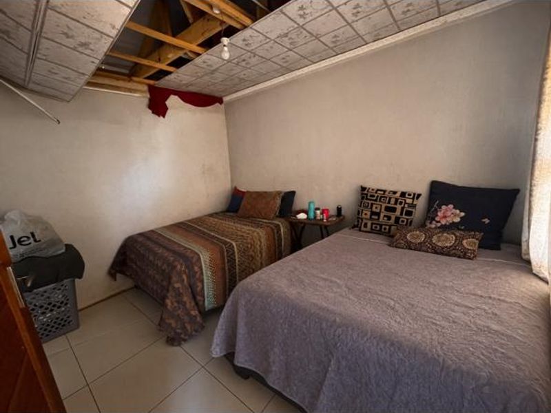 A bedroom featuring tiled flooring and exposed roof rafters due to missing ceiling panels, requiring significant repair and renovation.