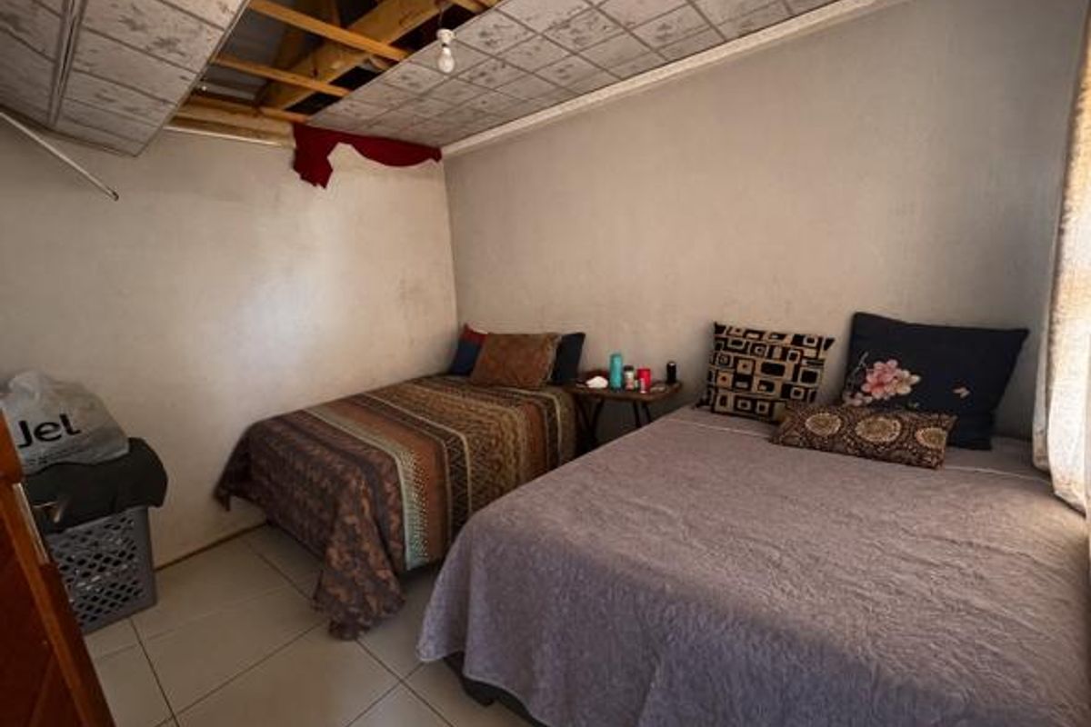 A bedroom featuring tiled flooring and exposed roof rafters due to missing ceiling panels, requiring significant repair and renovation.
