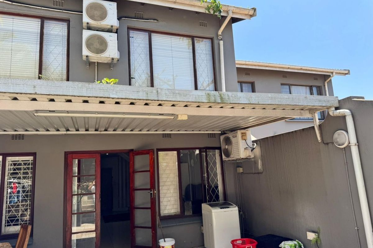 Rear exterior view of the townhouse featuring a covered patio area, multiple air conditioning units, and security-fitted timber doors.