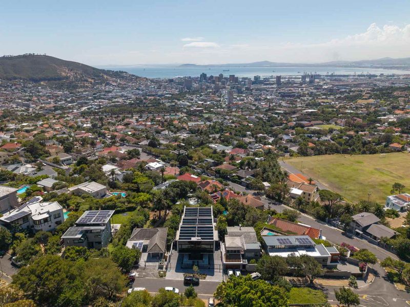 Aerial view of the property showing its location within the neighborhood, featuring solar panels on the roof and proximity to the city and coastline.
