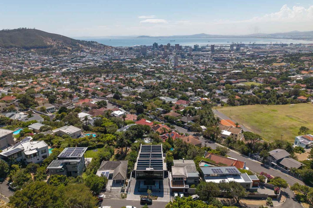 Aerial view of the property showing its location within the neighborhood, featuring solar panels on the roof and proximity to the city and coastline.