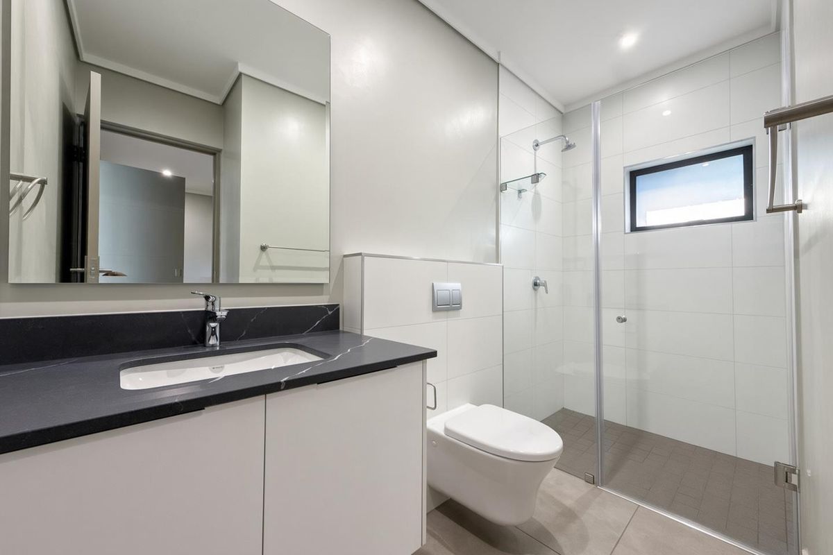Modern bathroom featuring a wall-mounted toilet, glass-enclosed shower, vanity with stone countertop, and clean, contemporary finishes.