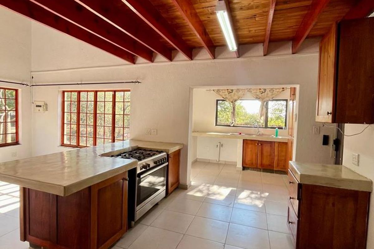Spacious kitchen featuring exposed timber ceiling beams, a large central island with a concrete countertop, built-in gas stove, and tiled flooring throughout.