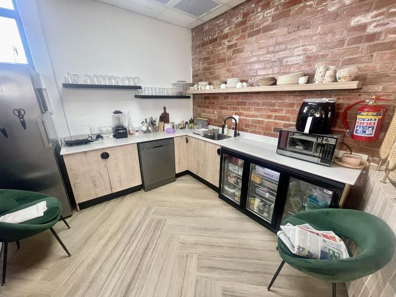 Modern kitchen featuring exposed brick walls, light wood-tone cabinetry, integrated dishwasher, glass-front under-counter refrigeration, and durable herringbone-patterned flooring.
