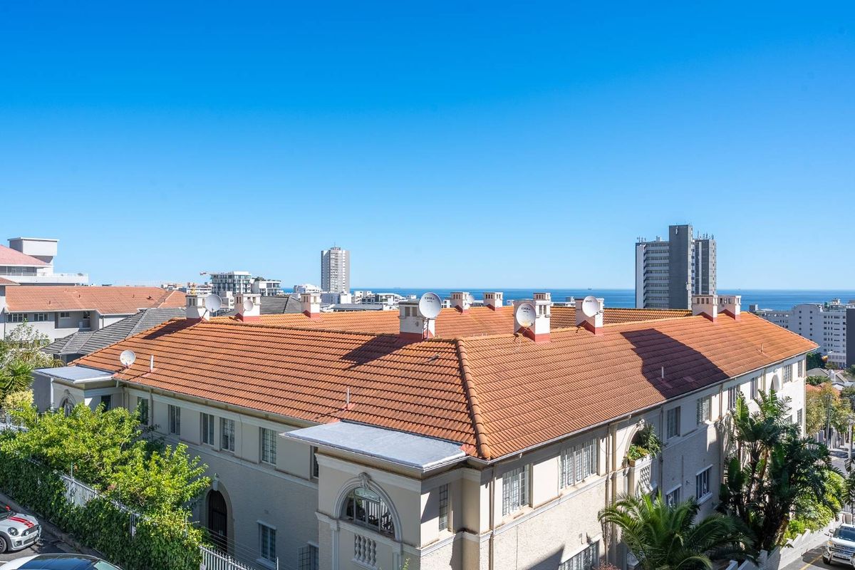 Aerial view of a multi-story apartment building with a tiled roof, featuring multiple satellite dishes and a clear view of the surrounding urban landscape.