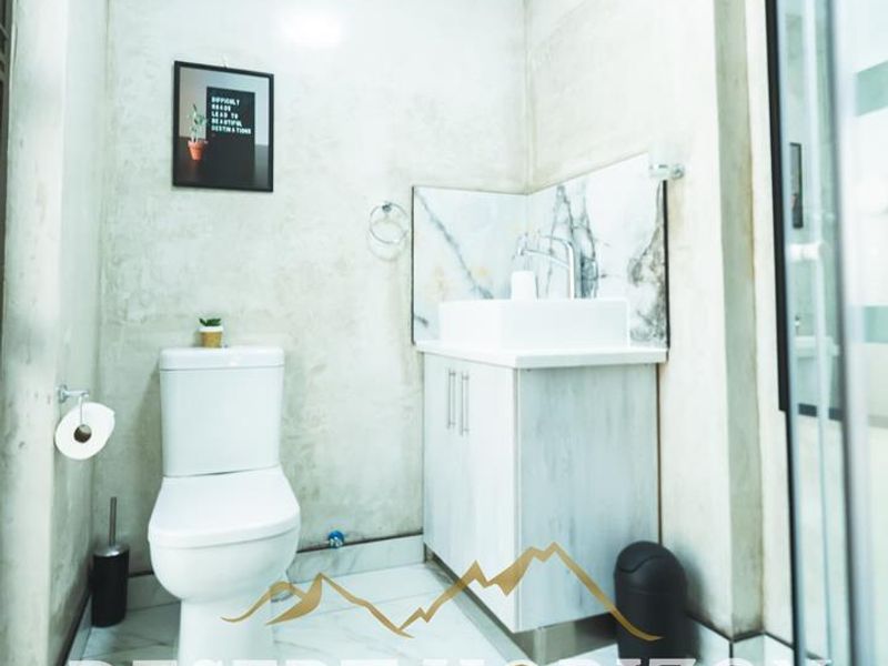 A compact bathroom featuring a modern vessel sink vanity, a white toilet, and a glass-enclosed shower with marble-look wall accents.