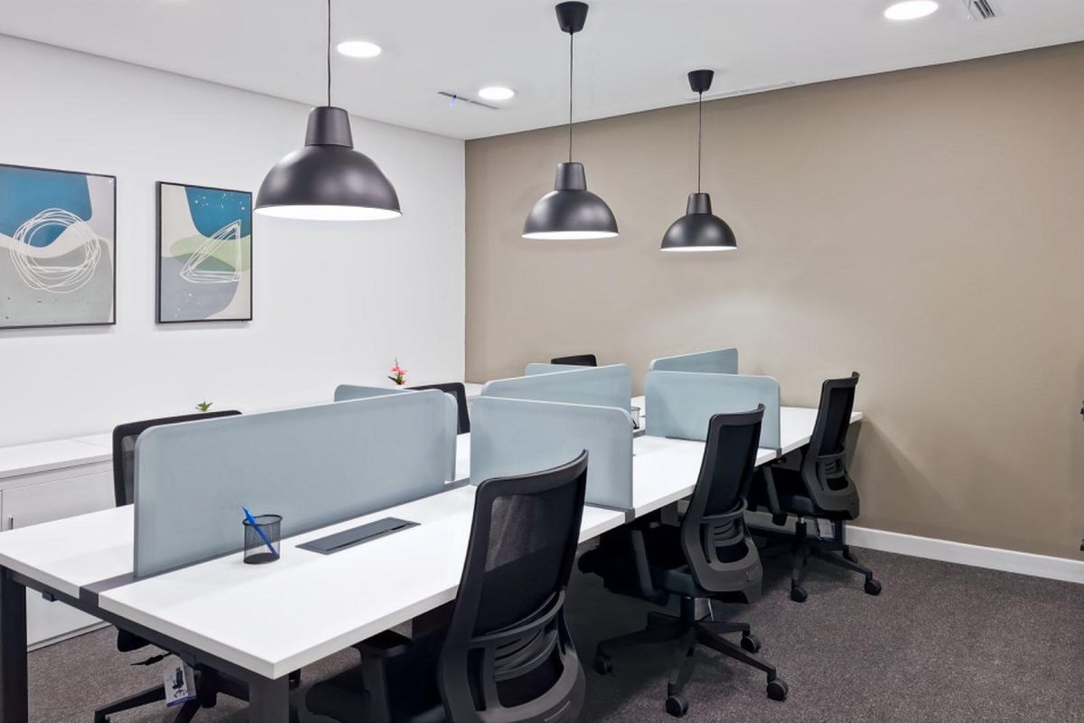 A modern, well-lit office space featuring organized workstations with integrated desk partitions, pendant lighting, and professional finishes.
