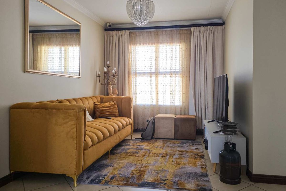 A well-maintained living room featuring tiled flooring, decorative ceiling cornicing, and a central crystal chandelier, providing a comfortable and inviting atmosphere.