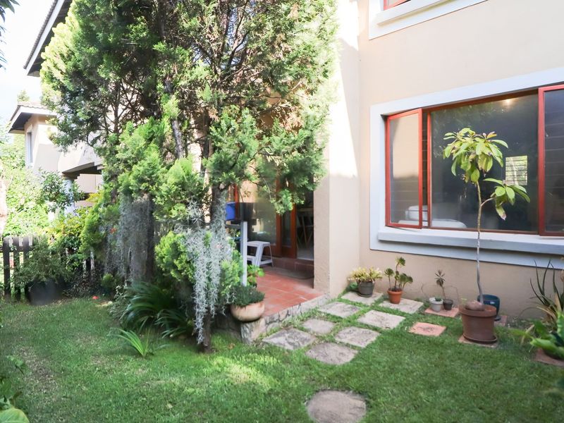 A view of the rear garden area featuring a small lawn, paved stepping stones, and a sliding window leading into the home.