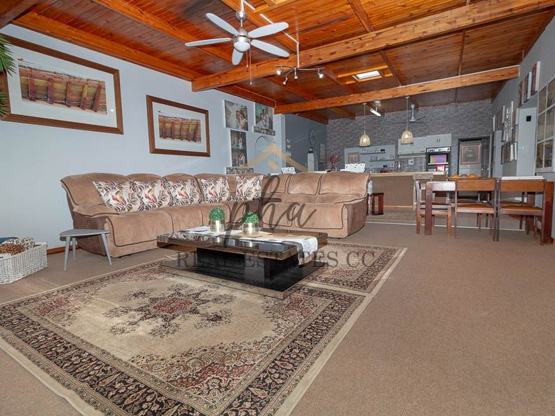 Spacious open-plan living and dining area featuring a high exposed timber beam ceiling, skylight, and a stone feature wall in the kitchen.