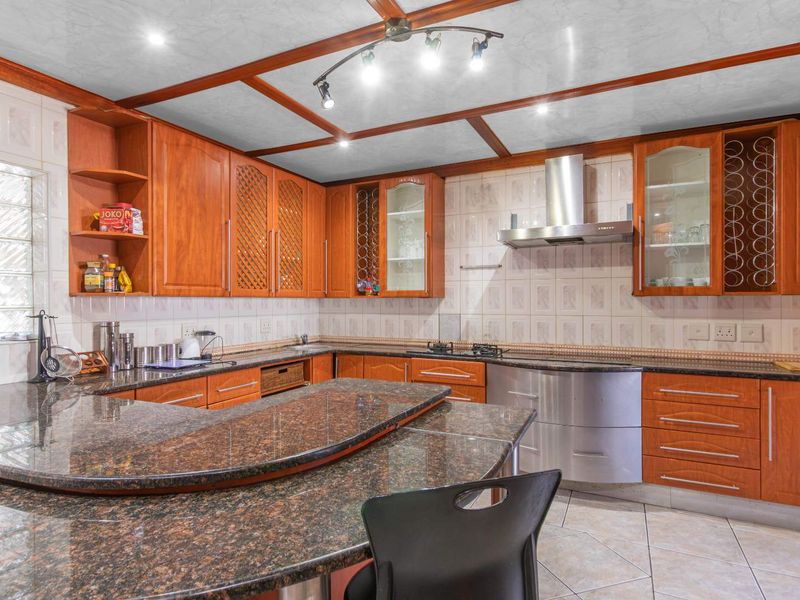A spacious kitchen featuring extensive wooden cabinetry, granite countertops, a built-in hob with stainless steel extractor, and a distinctive coffered ceiling design.