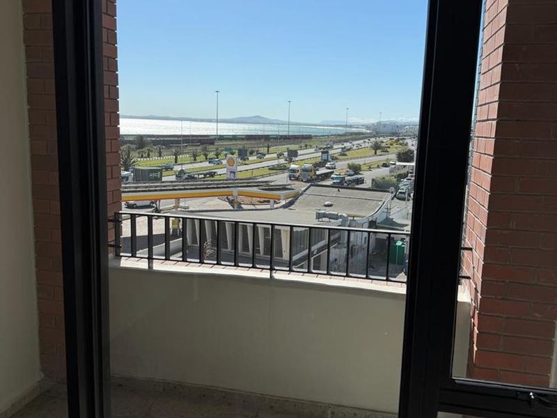 A private balcony featuring tiled flooring and a metal railing, offering an elevated view of the surrounding area and coastal landscape.