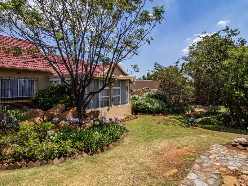 A well-maintained rear garden featuring a stone pathway, established trees, landscaped flower beds with brick edging, and a view of the house exterior.