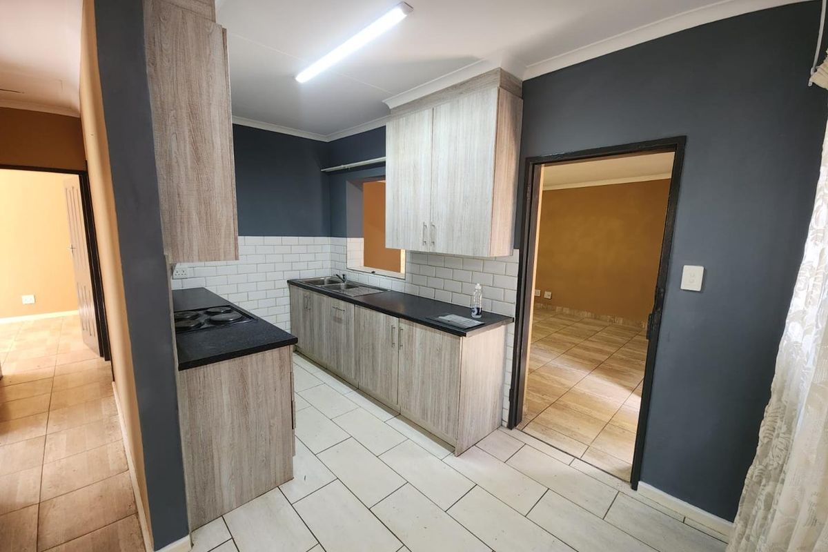 A clean, functional kitchen featuring light wood-grain cabinetry, dark countertops, subway tile backsplash, and neutral ceramic floor tiles.