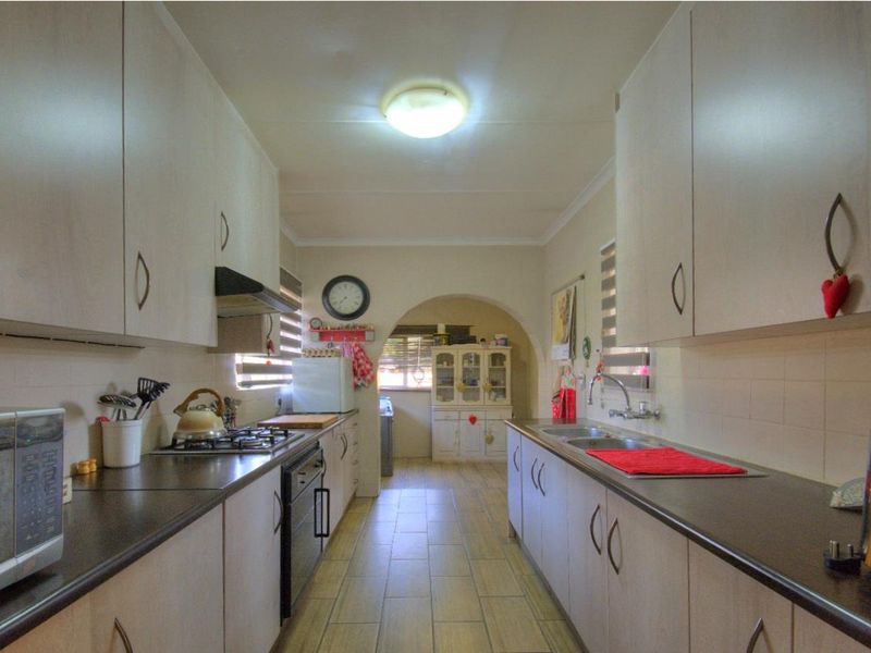 A functional galley-style kitchen featuring built-in cabinetry, laminate countertops, a gas hob, and a double sink with tiled flooring.