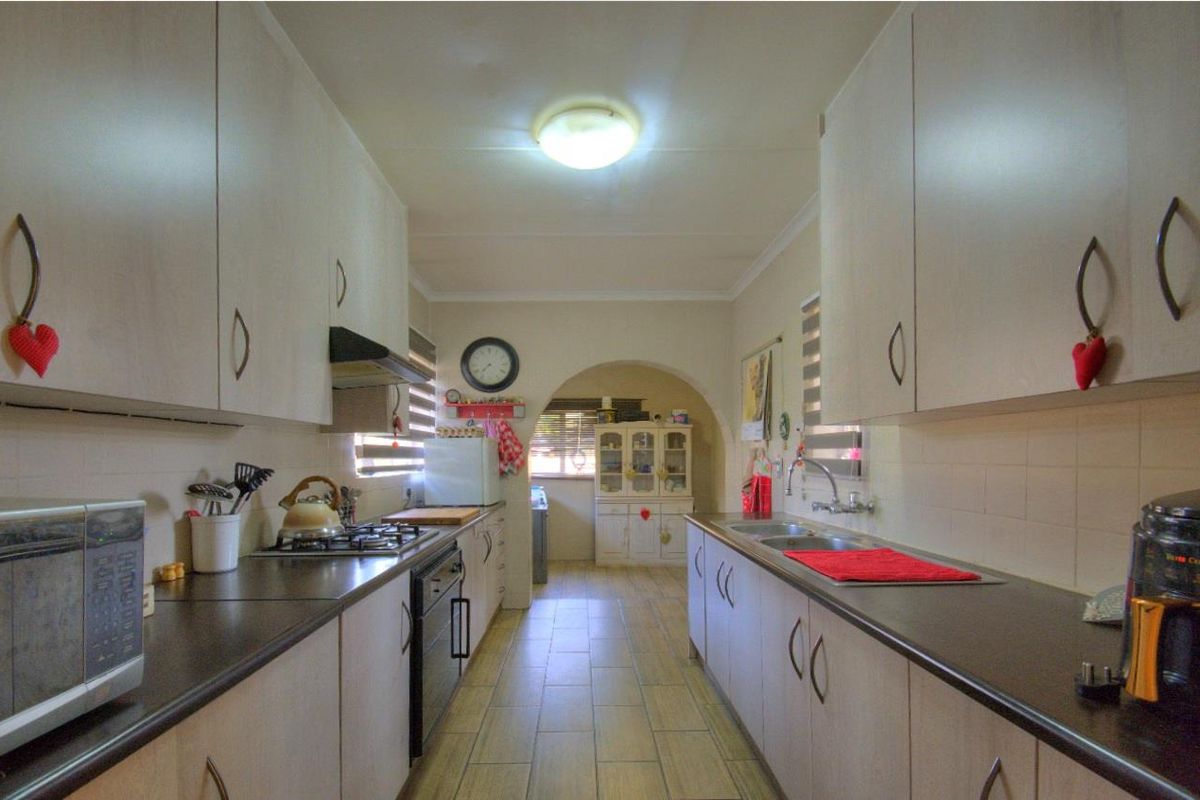 A functional galley-style kitchen featuring built-in cabinetry, laminate countertops, a gas hob, and a double sink with tiled flooring.