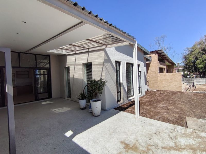 A spacious covered patio featuring a modern metal pergola, tiled flooring, and large glass sliding doors leading into the interior living space.