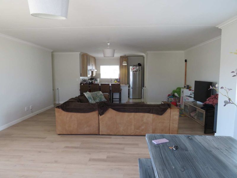 An open-plan living and kitchen area featuring light-toned laminate flooring, neutral walls, and a functional kitchen layout with a central island.