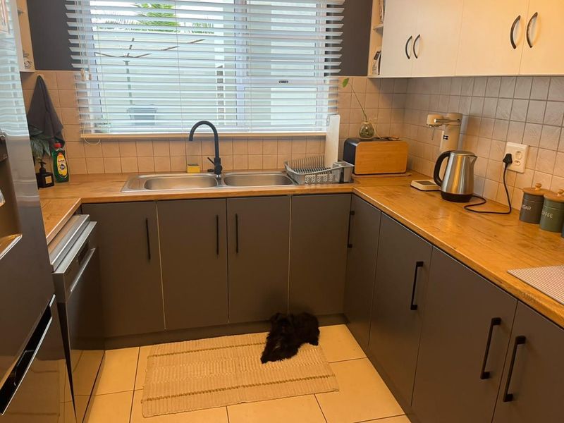 A functional kitchen featuring grey cabinetry, wood-look countertops, a double bowl sink with a modern black tap, and tiled splashbacks.