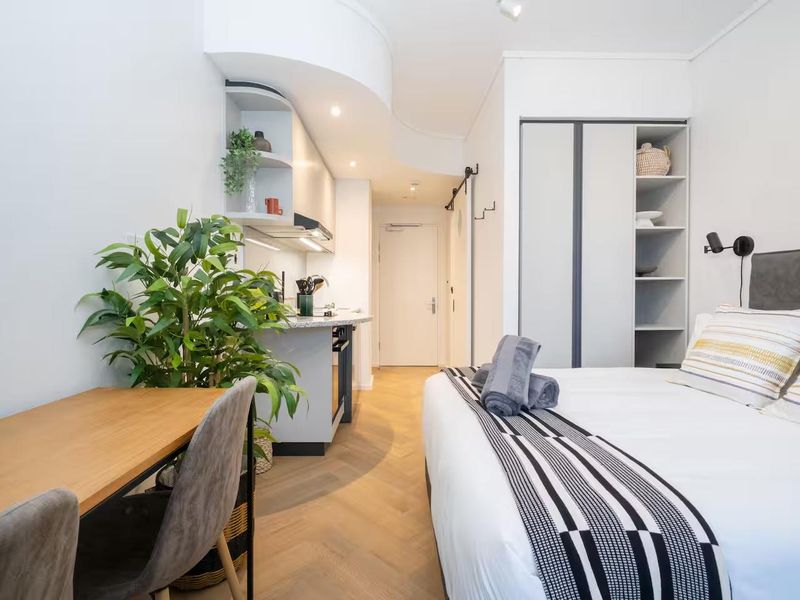 A modern open-plan studio apartment featuring high-quality herringbone timber flooring, a compact built-in kitchenette, and integrated wardrobe storage.