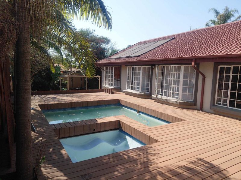 Outdoor entertainment area featuring a swimming pool and integrated spa surrounded by timber decking, with solar panels installed on the tiled roof.